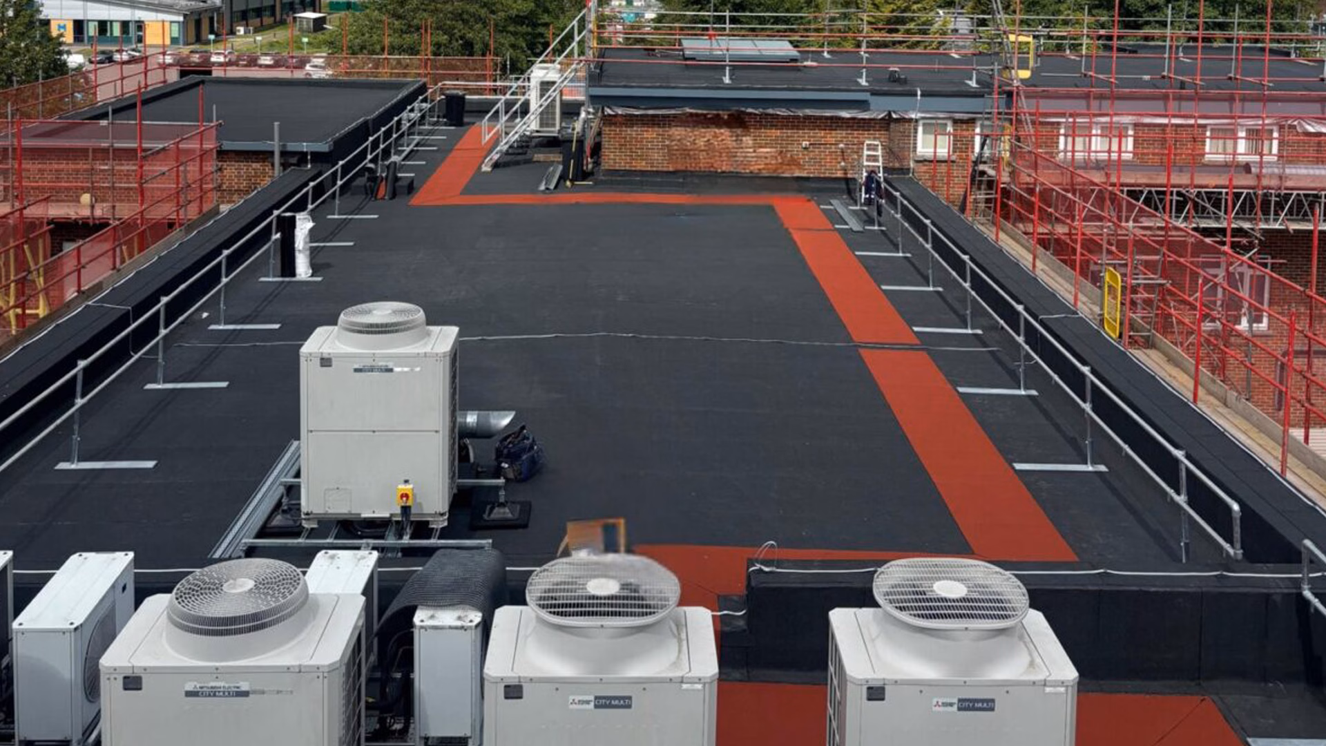 Completed commercial flat roof refurbishment at MRC Harwell Oxfordshire showing Langley TA-25 felt roofing system, red mineral walkway routes, rooftop plant equipment and LangGuard free-standing safety handrail system