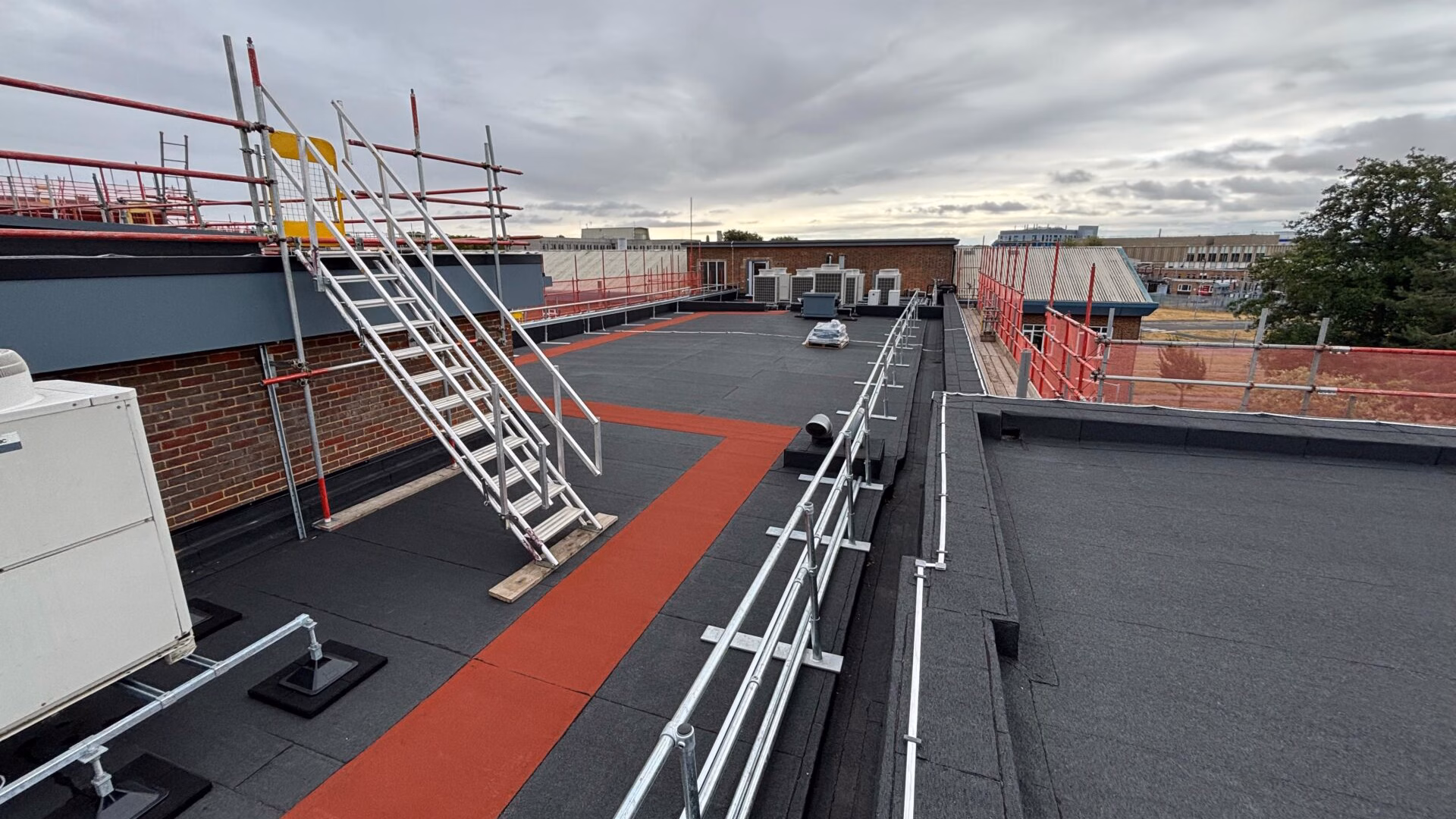 Commercial flat roof refurbishment at MRC Harwell Oxfordshire showing LangGuard free-standing guardrail system and designated red mineral felt walkways installed on new felt roofing system.