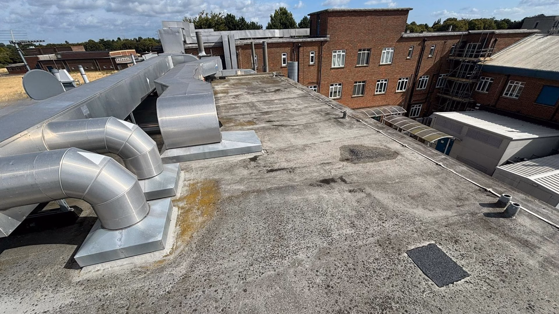 Existing flat roof condition at MRC Harwell Oxfordshire prior to commercial roof refurbishment showing weathered waterproofing and rooftop plant equipment.