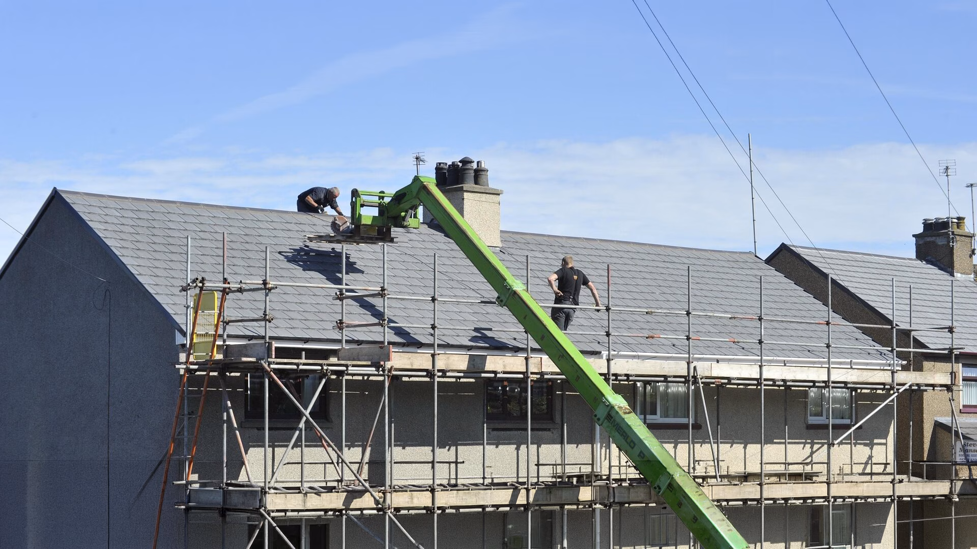 Men on roof with scaffolding on the front of the building.